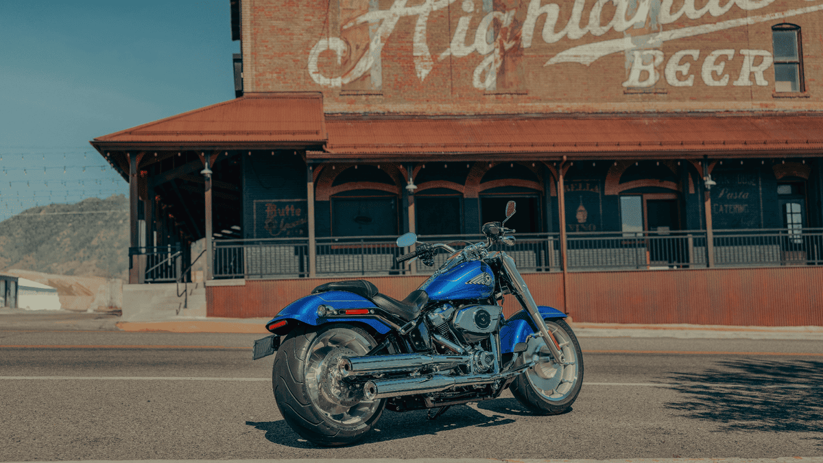 Blue 2025 Harley-Davidson® Fat Boy® parked on a sunny street near Deer Park, TX, showcasing its wide rear tire and bold chrome styling.