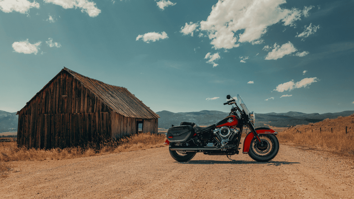 2025 Harley-Davidson® Heritage Classic in red and black parked near a rustic barn in Deer Park, TX, blending vintage charm with touring comfort.