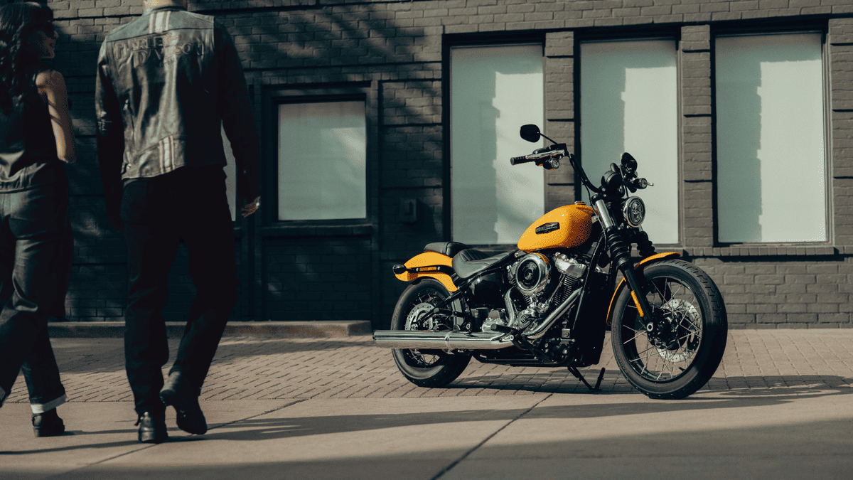 2025 Harley-Davidson® Street Bob® in bright yellow parked curbside as riders approach near Deer Park, TX, showcasing its minimalist bobber look.