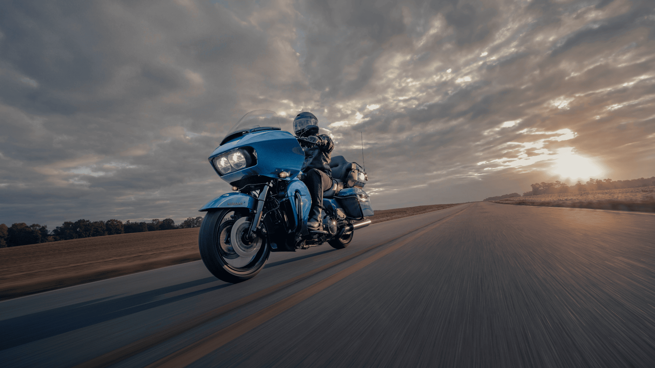 A rider on a blue motorcycle cruising down a scenic road near League City, TX, showcasing the 2024 Harley-Davidson® Road Glide® Limited.